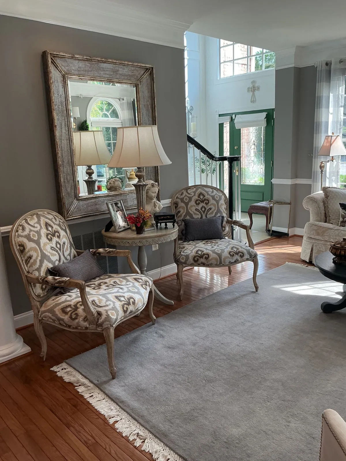 Living room with patterned armchairs, a large framed mirror and a green entry door
